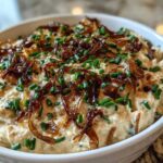 Close-up of a creamy homemade onion dip topped generously with crispy caramelized onions and fresh chopped chives.