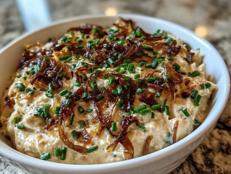 Close-up of a creamy homemade onion dip topped generously with crispy caramelized onions and fresh chopped chives.