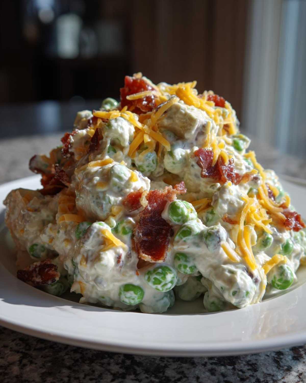 A mound of creamy pea salad mixed with dressing, topped generously with shredded cheddar cheese and crispy bacon pieces.