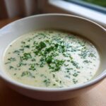 A close-up of a bowl of creamy potato leek soup garnished generously with fresh chopped chives.