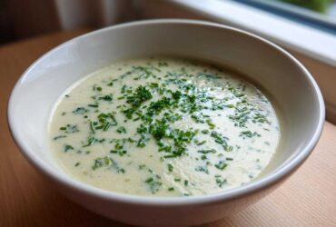 A close-up of a bowl of creamy potato leek soup garnished generously with fresh chopped chives.