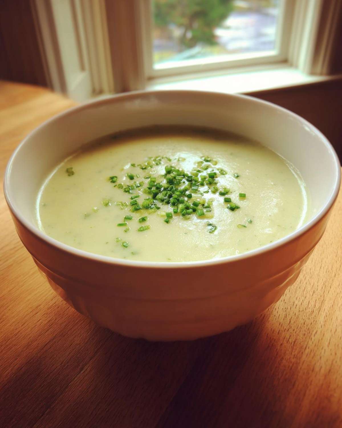 A creamy bowl of potato leek soup topped with freshly chopped chives, set on a wooden table.