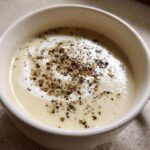 Close-up of creamy roasted cauliflower soup topped with a swirl of cream and cracked black pepper.