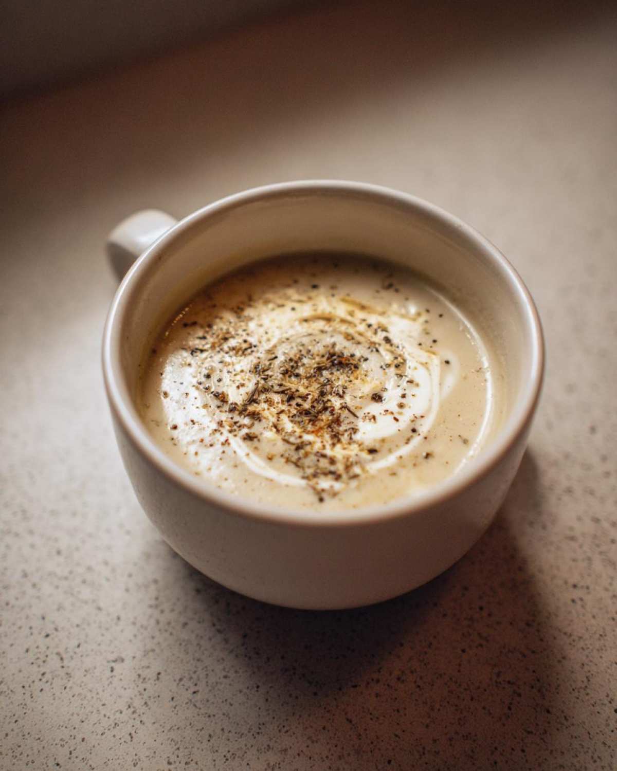 Close-up of creamy roasted cauliflower soup topped with a swirl of cream and cracked pepper.