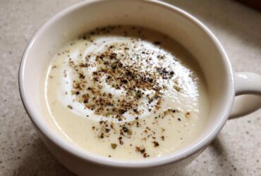 Close-up of creamy roasted cauliflower soup topped with a swirl of cream and cracked black pepper.