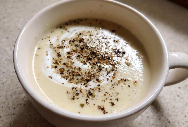 Close-up of creamy roasted cauliflower soup topped with a swirl of cream and cracked black pepper.