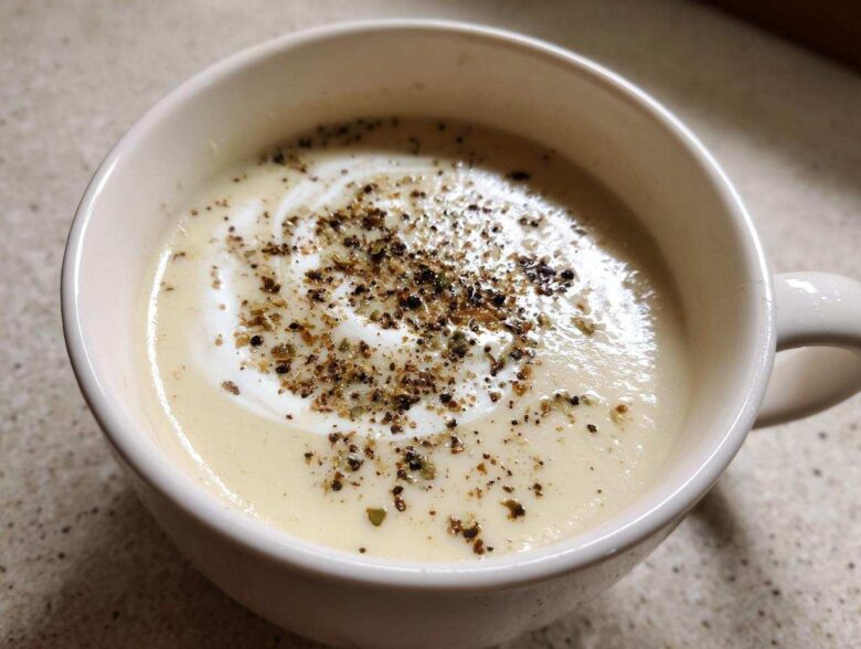 Close-up of creamy roasted cauliflower soup topped with a swirl of cream and cracked black pepper.