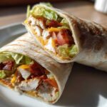 Two halves of a grilled chicken bacon ranch wrap, showing chunks of chicken, bacon, cheese, and lettuce.