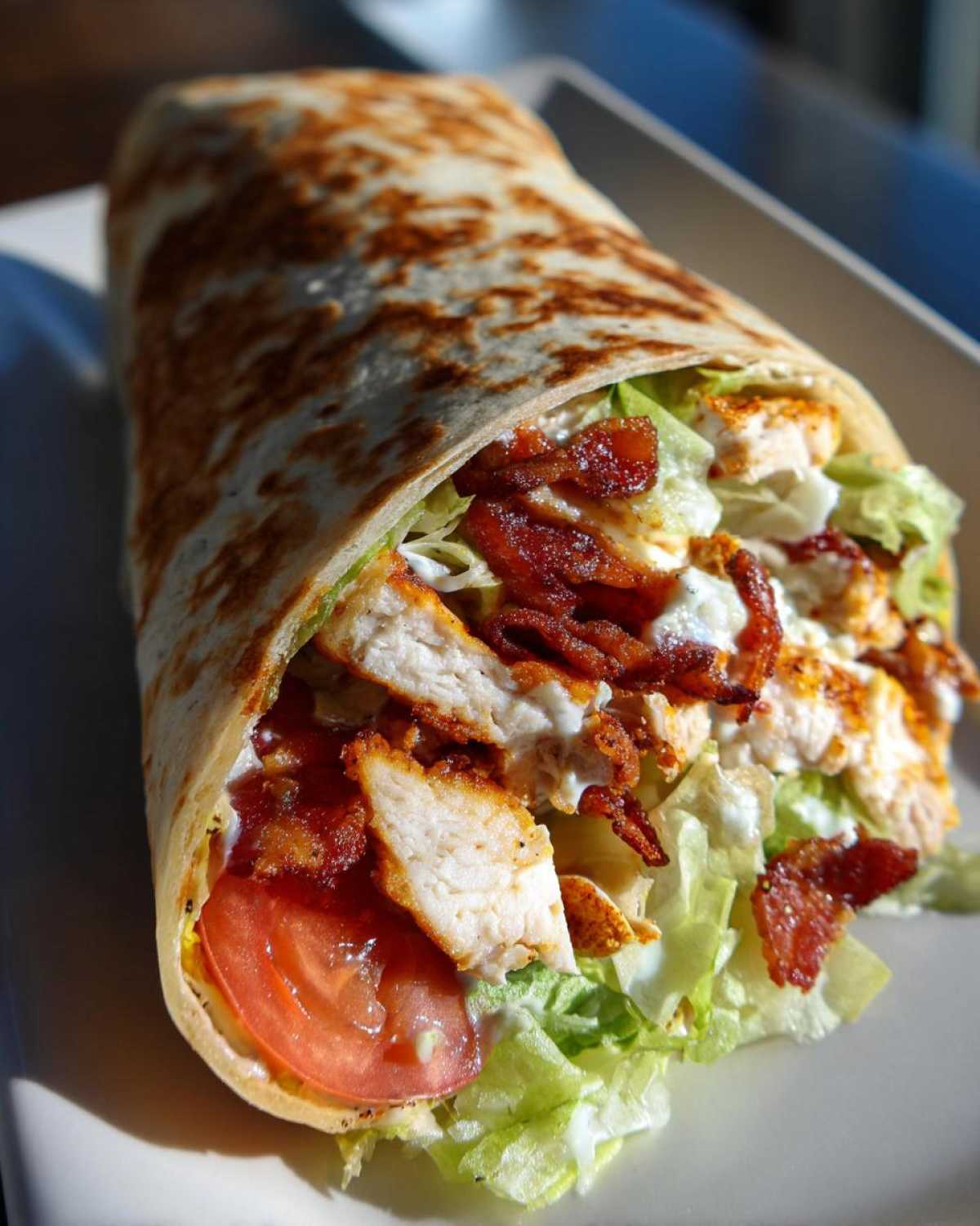 A close-up view of a toasted tortilla stuffed with chicken, bacon, lettuce, tomato, and ranch dressing, showing the ingredients of the chicken bacon ranch wrap.