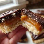 Close-up of a twix cookie broken in half showing shortbread base, flowing caramel filling, and chocolate topping.