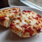 Close-up of two halves of an English Muffin Pizza with bubbly, melted mozzarella cheese and tomato sauce.
