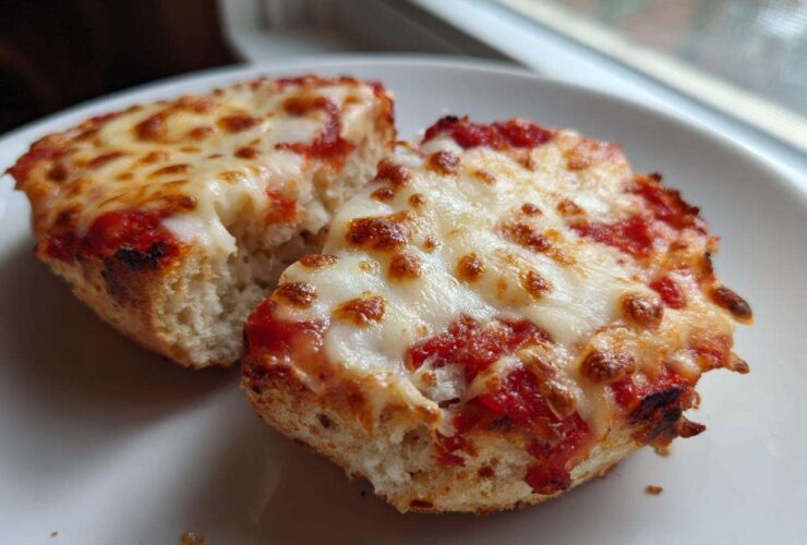 Close-up of two halves of an English Muffin Pizza with bubbly, melted mozzarella cheese and tomato sauce.