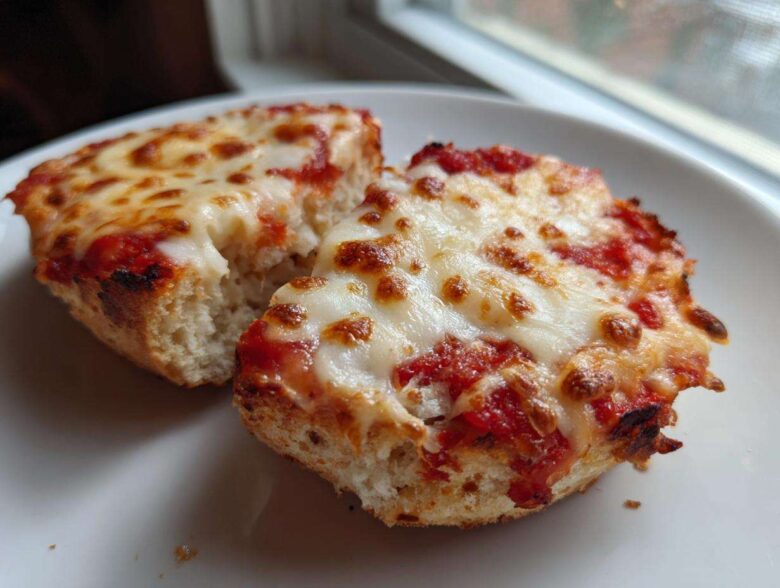 Close-up of two halves of an English Muffin Pizza with bubbly, melted mozzarella cheese and tomato sauce.
