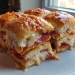 Close-up of four gooey pepperoni pizza sliders stacked on a white plate, featuring melted cheese.