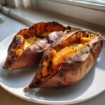Two perfectly cooked baked sweet potato halves with fluffy orange insides on a white plate.