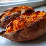 Close-up of two fluffy baked sweet potato halves with bright orange, mashed interiors on a white plate.