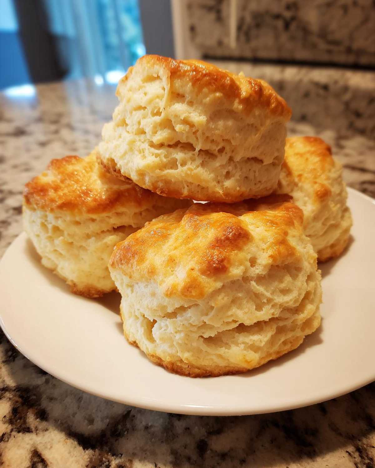 A stack of four tall, fluffy, golden-brown scones piled on a white plate.