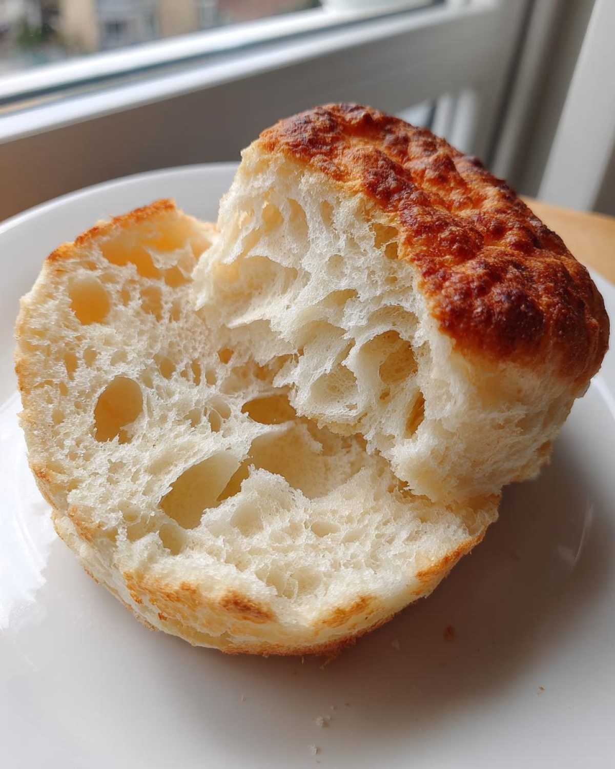 Close-up of a perfectly cooked English muffin split in half, showing its airy, craggy interior.