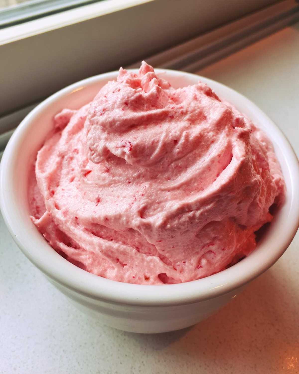 Close-up of fluffy pink strawberry cheesecake dip swirled high in a small white bowl.