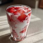 Close-up of a glass containing fresh strawberry milk, showing swirls of white milk and bright red sliced strawberries.