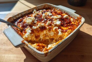 A square, white baking dish filled with hot, bubbly street corn dip, topped with cotija cheese and chili powder.