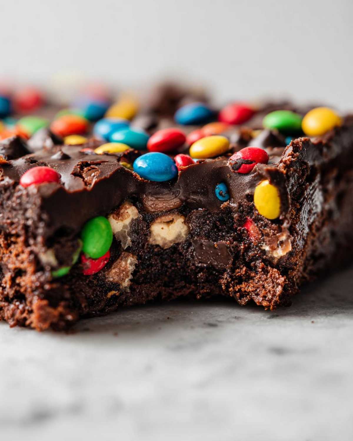 Close-up of a fudgy cosmic brownies piece topped with chocolate frosting and colorful candy-coated chocolates.