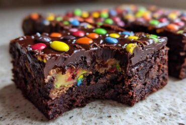 Close-up of a fudgy cosmic brownie square with a bite missing, revealing colorful candy filling and chocolate frosting.