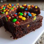 Close-up of a fudgy cosmic brownie slice topped with chocolate frosting and colorful candy-coated chocolates.