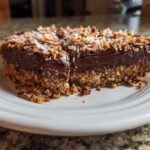 A rich slice of German chocolate pie showing a thick chocolate layer and a coconut-pecan crust, topped with toasted coconut.