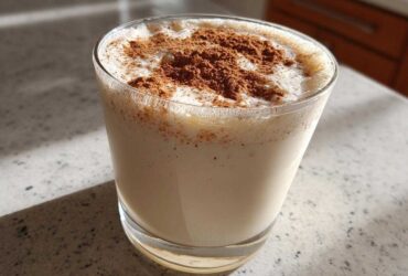 A glass of creamy, chilled coquito topped generously with ground cinnamon spice.