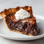 A close-up of a rich, gooey slice of hot fudge pie topped with a dollop of fresh whipped cream.