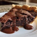 Close-up of a slice of hot fudge pie with a gooey, melted chocolate center oozing onto a white plate.