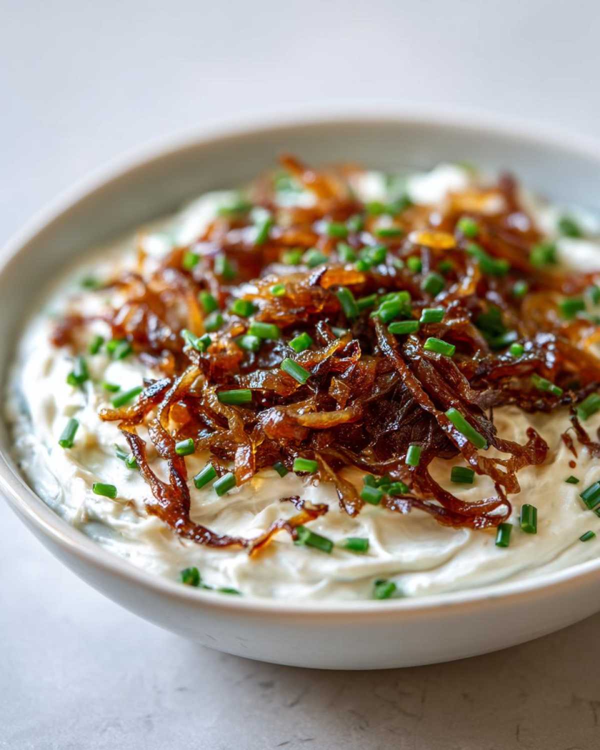 Close-up of a creamy onion dip topped generously with caramelized onions and fresh chopped chives.