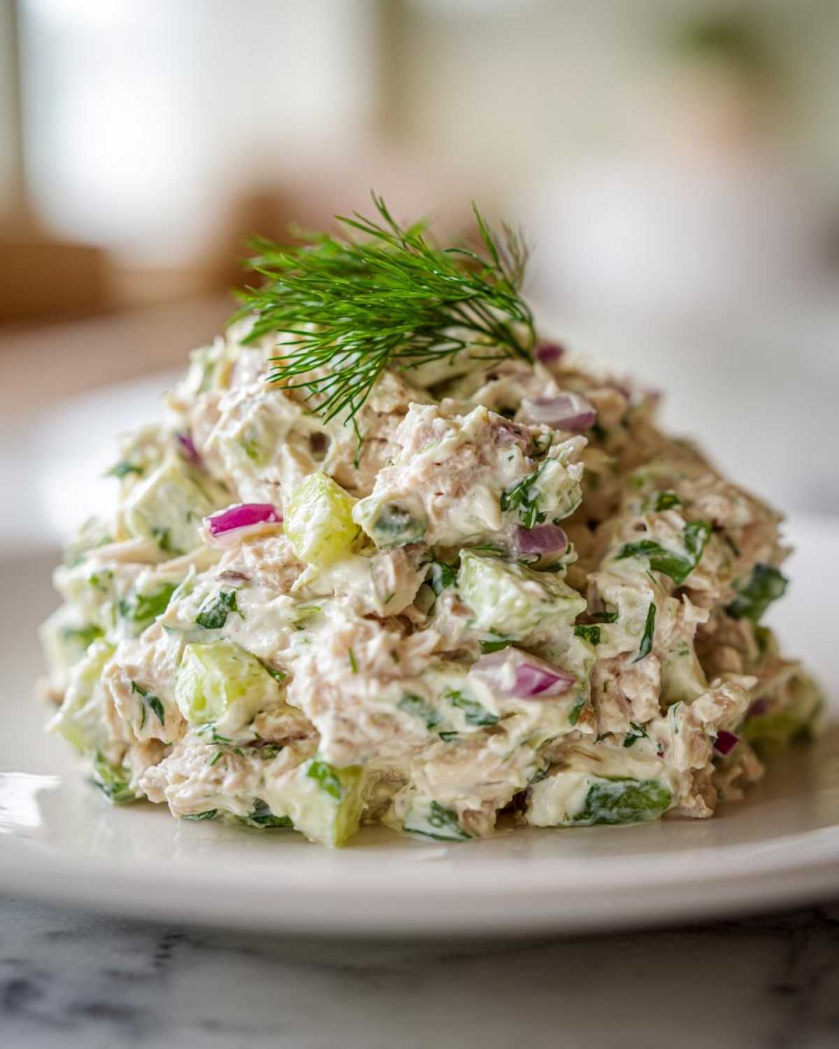 A scoop of creamy, chunky healthy tuna salad mixed with cucumber and red onion, topped with fresh dill.
