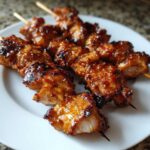 Close-up of several glistening, glazed honey garlic chicken skewers resting on a white plate.