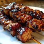 Close-up of several glazed, caramelized honey garlic chicken skewers resting on a white plate.