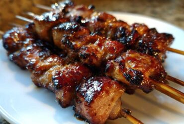 Close-up of several glazed, caramelized honey garlic chicken skewers resting on a white plate.