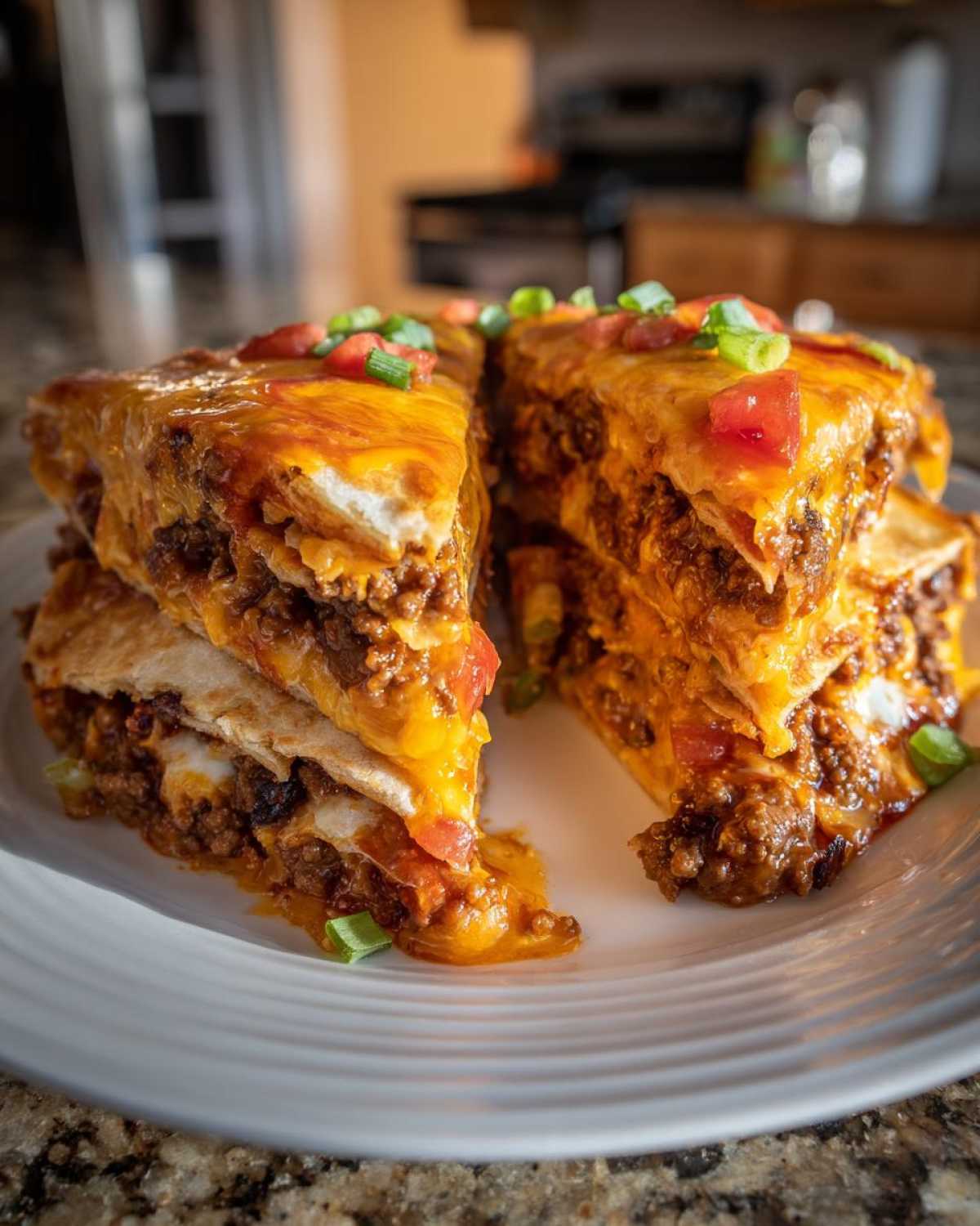 Two stacked slices of a rich mexican pizza, layered with seasoned ground beef and melted cheddar cheese, topped with diced tomatoes and green onions.
