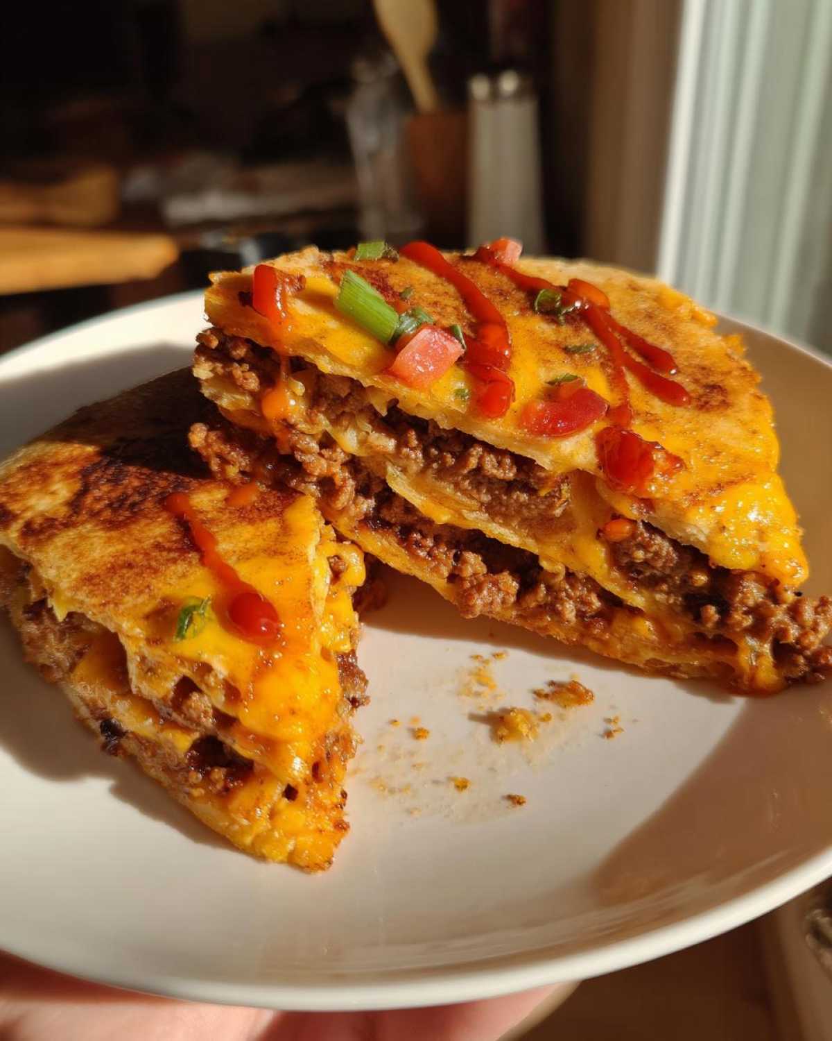 Two halves of a homemade mexican pizza stacked with seasoned ground beef and melted cheese, drizzled with sauce.