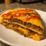 A cross-section view of a delicious Mexican pizza slice showing layers of seasoned ground beef, melted cheddar cheese, and topped with salsa and onions.