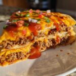 A thick, layered slice of homemade Mexican pizza featuring seasoned ground beef, melted cheese, and topped with salsa and green onions.