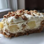 A close-up slice of rich, creamy million dollar pie with pineapple chunks and a nutty topping.