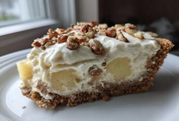 A close-up slice of rich, creamy million dollar pie with pineapple chunks and a nutty topping.