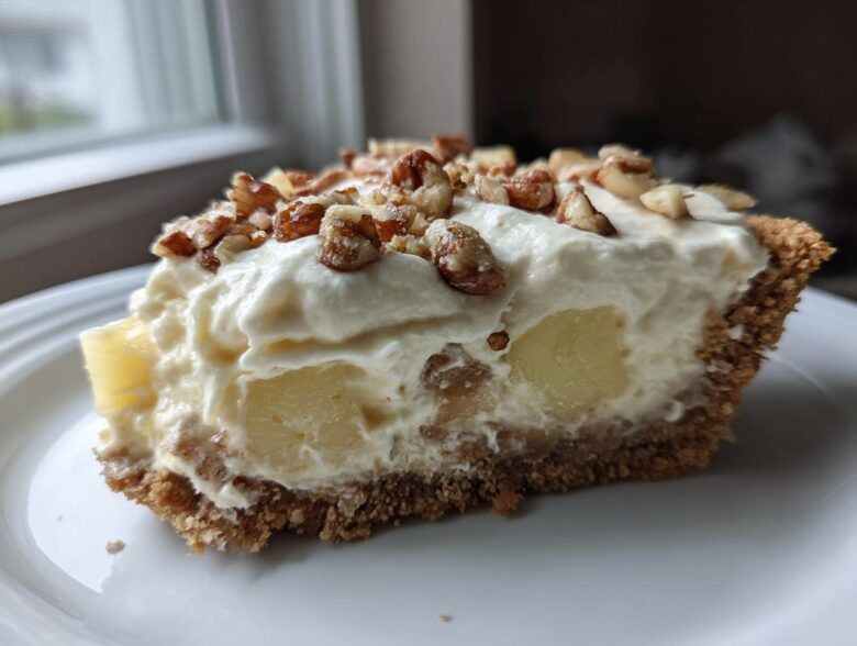 A close-up slice of rich, creamy million dollar pie with pineapple chunks and a nutty topping.