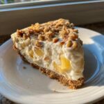 A tempting slice of million dollar pie featuring a graham cracker crust, creamy filling with pineapple chunks, and a crunchy pecan topping.