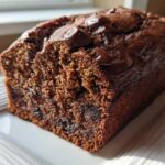 A close-up of a freshly baked, dark chocolate banana bread loaf topped with melted chocolate chips.