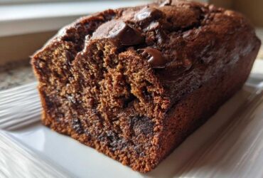 A close-up of a freshly baked, dark chocolate banana bread loaf topped with melted chocolate chips.