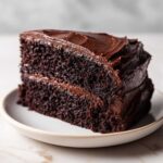 Close-up of a thick slice of moist chocolate cake layered with dark chocolate frosting.