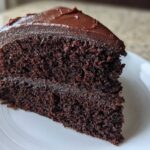 Close-up of a thick slice of moist chocolate cake layered with dark chocolate frosting.
