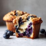 Close-up of a blueberry cream cheese muffin cut in half showing the melted cream cheese center and juicy blueberries.